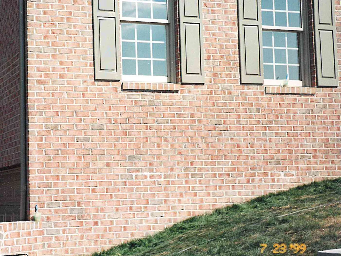 A brick wall of the house photographed in 1999 after the work, two shuttered windows above and a low garden wall at its foot