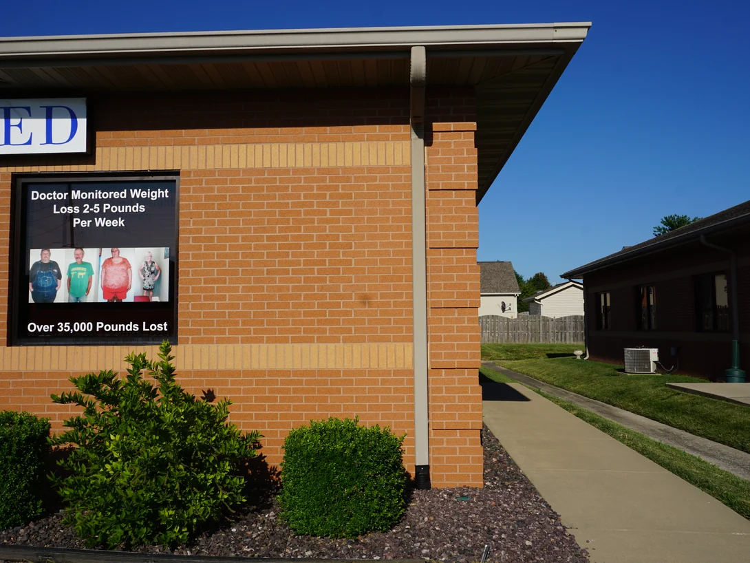 An outside corner of the office in 2019, the buff soldier band carrying around the return onto the end wall below a tenant sign, with a projecting brick pier at the corner
