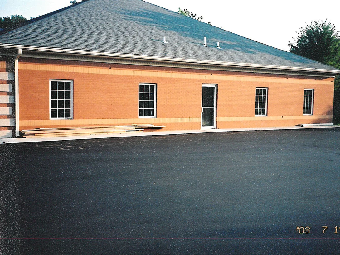 The office in 2003 from the opposite direction, the soldier band running as one tan course below the windows and past a glazed door, with fresh asphalt in front of it