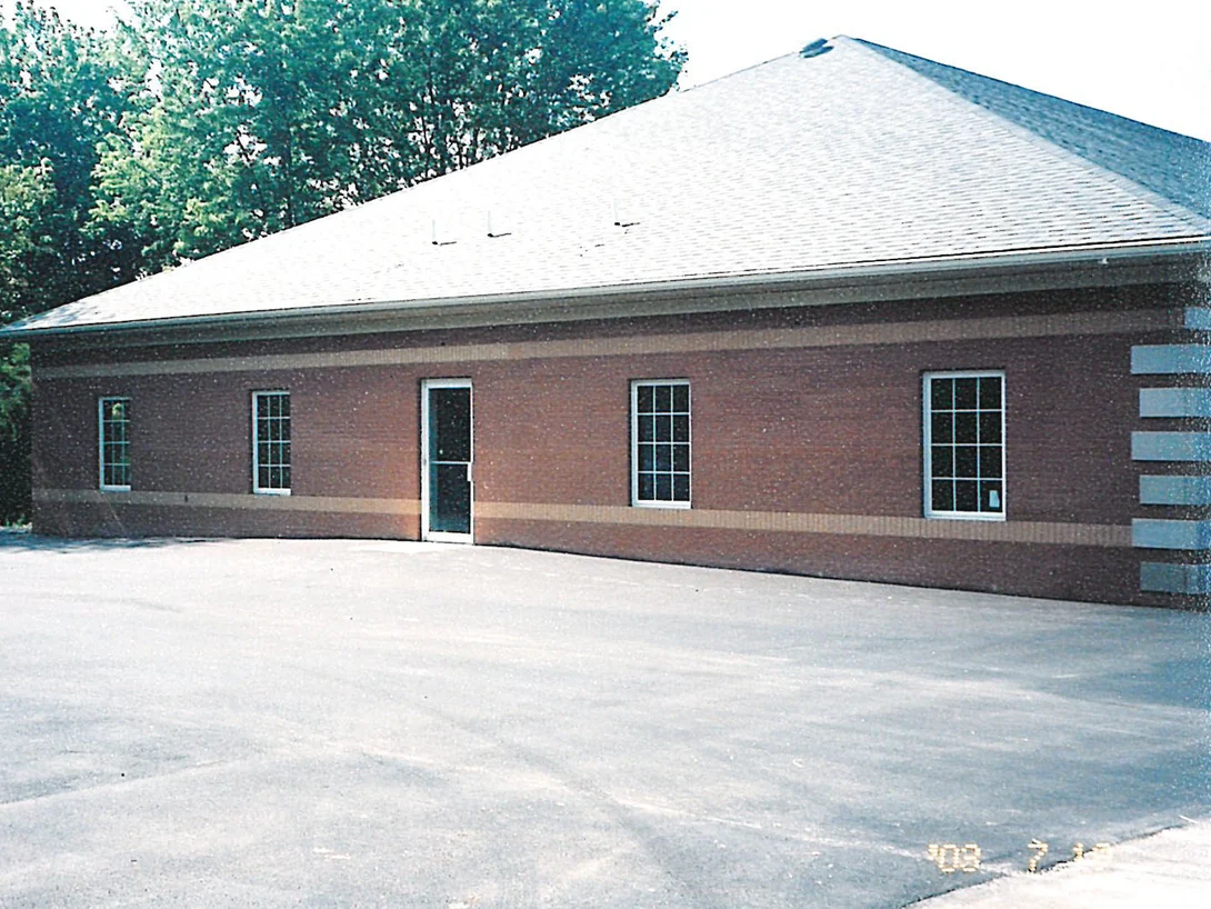 A single-story office in 2003 seen along its long wall, deep red brick with a buff soldier band below the window sills that drifts from cream to tan across the elevation