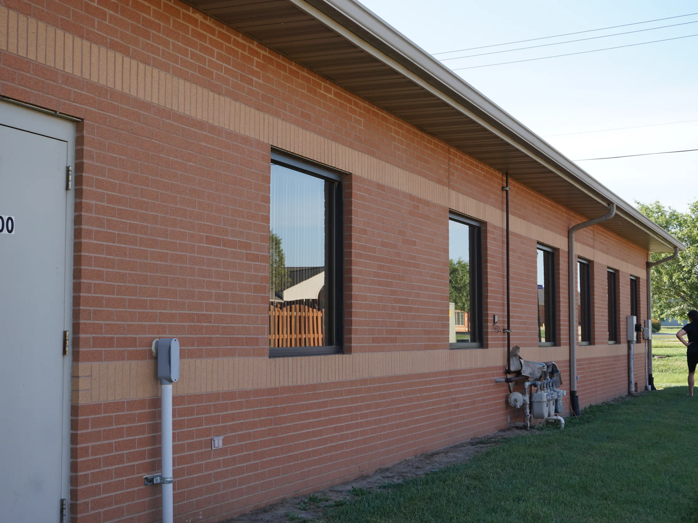 The long side wall of the office in 2019, a buff soldier band running level below the windows and a second buff course under the eaves, the brick between them an even orange red