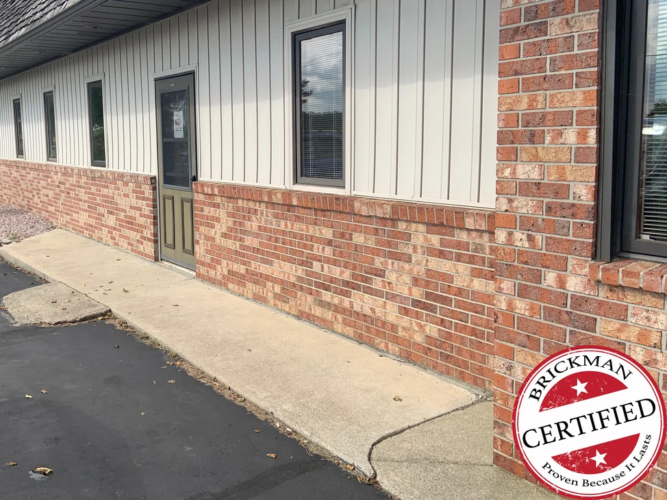 The side wall of the clinic in 2019, red blend brick below the siding from the door to the corner pier, with the Brickman Certified stamp in the corner.