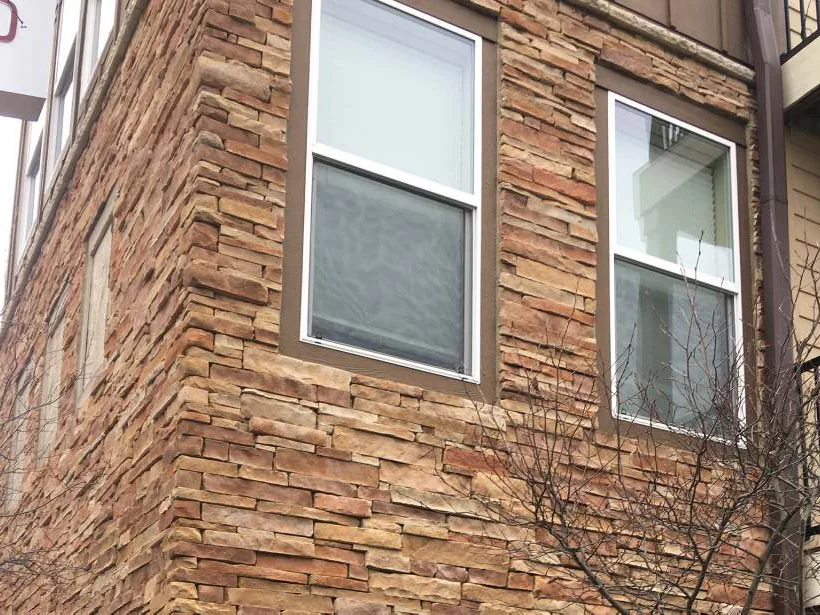 An outside corner beside a balcony in 2021, two windows set in stacked stone that reads as one warm tan and red brown range up to the return