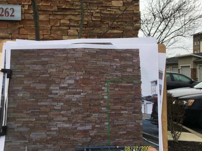 A 2009 print of a stained wall held against that wall in 2021, the courses in the print lining up with the courses behind it and the tone matching across the join