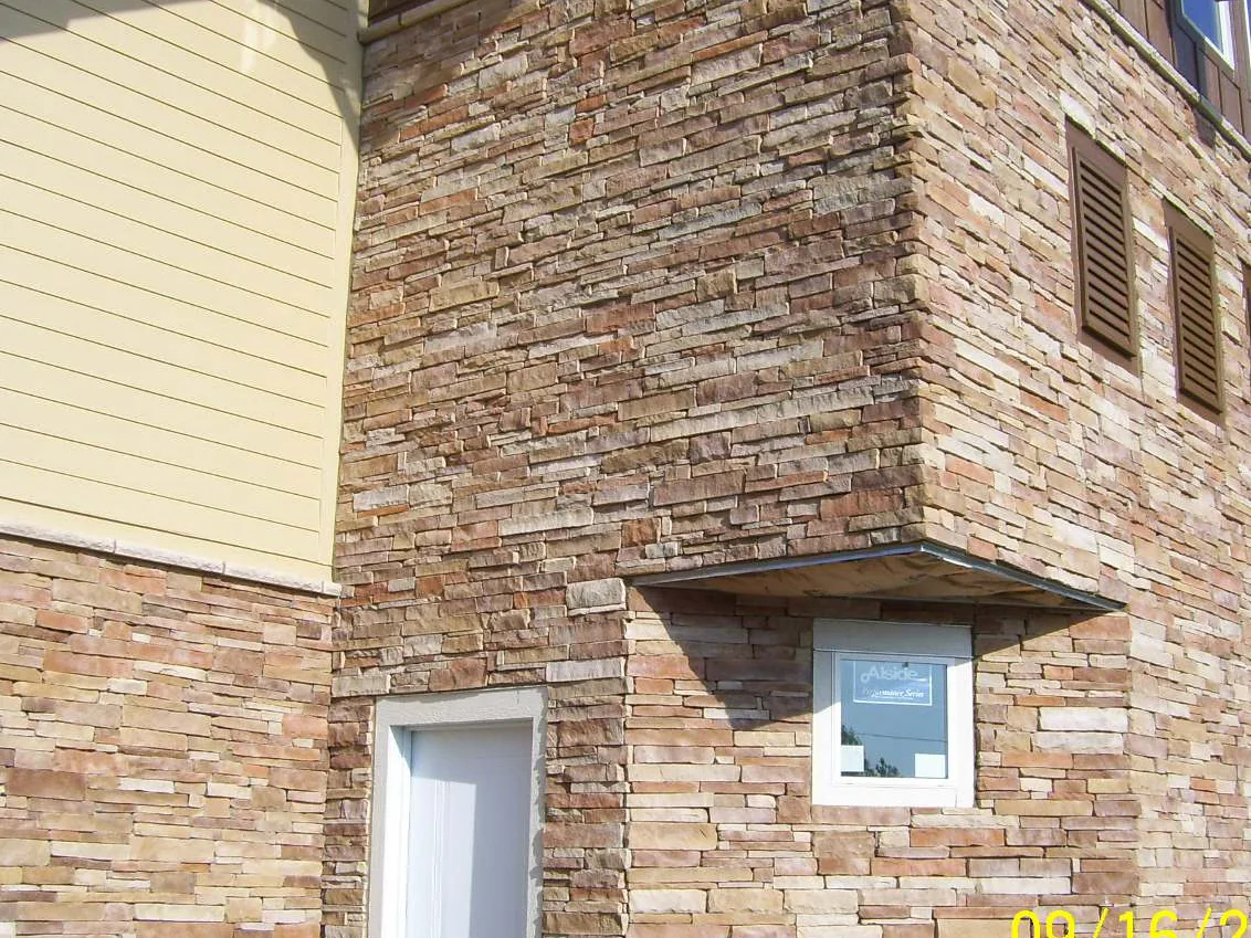 A projecting stone corner in 2009 above a service door, the stacked stone running from cream and pale tan to light pink with a camera date burned into the bottom right