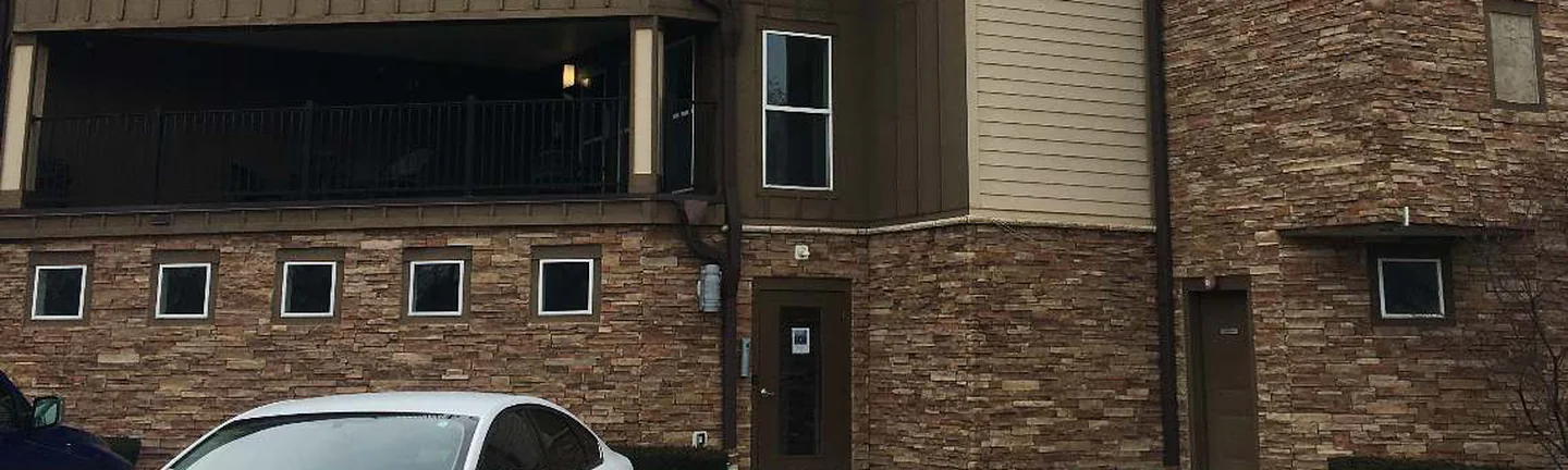 The stone base course of the Ohio apartment building in 2021, running under three storeys of balconies and board siding, with a parked car at the kerb