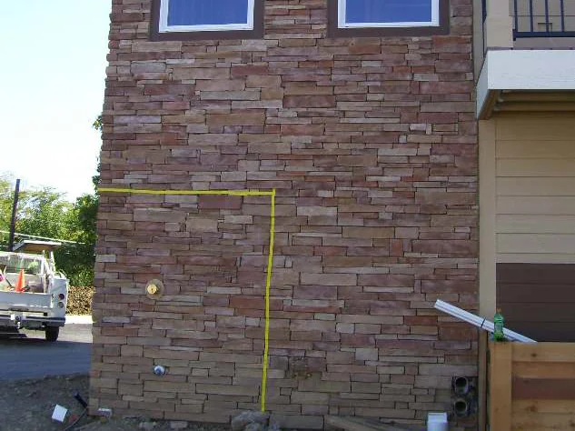 The same taped test area in 2009 once it had been stained, the stone inside the yellow line a deeper red brown, a truck and a traffic cone in the lot behind