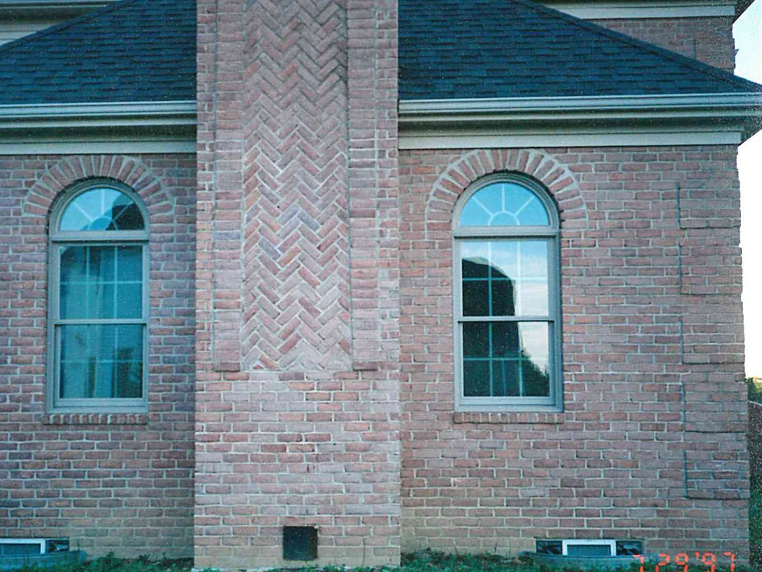 The front of the house in 1997, a projecting chimney breast with a herringbone brick panel standing between two arched windows, the brick around it mottled pink and mauve
