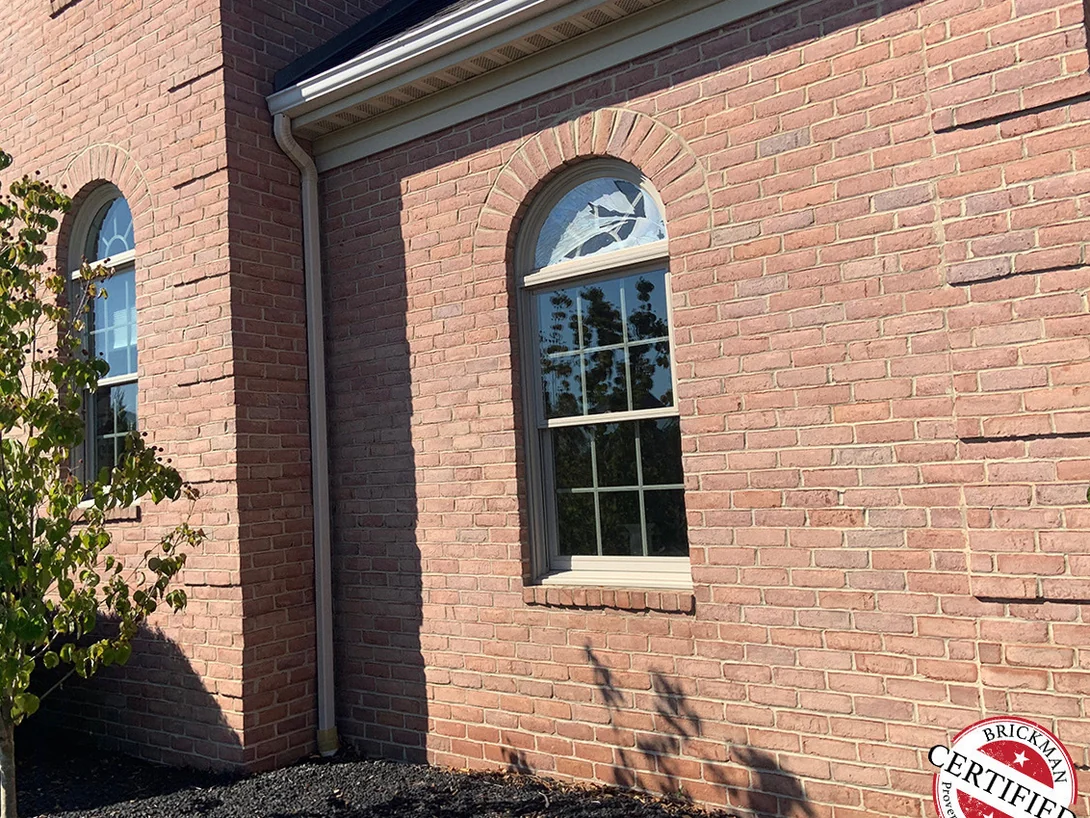 A side wall of the house in 2019 with an arched window under a radiating brick arch, the brick reading as one even red range across the whole elevation, with the certification stamp in the corner