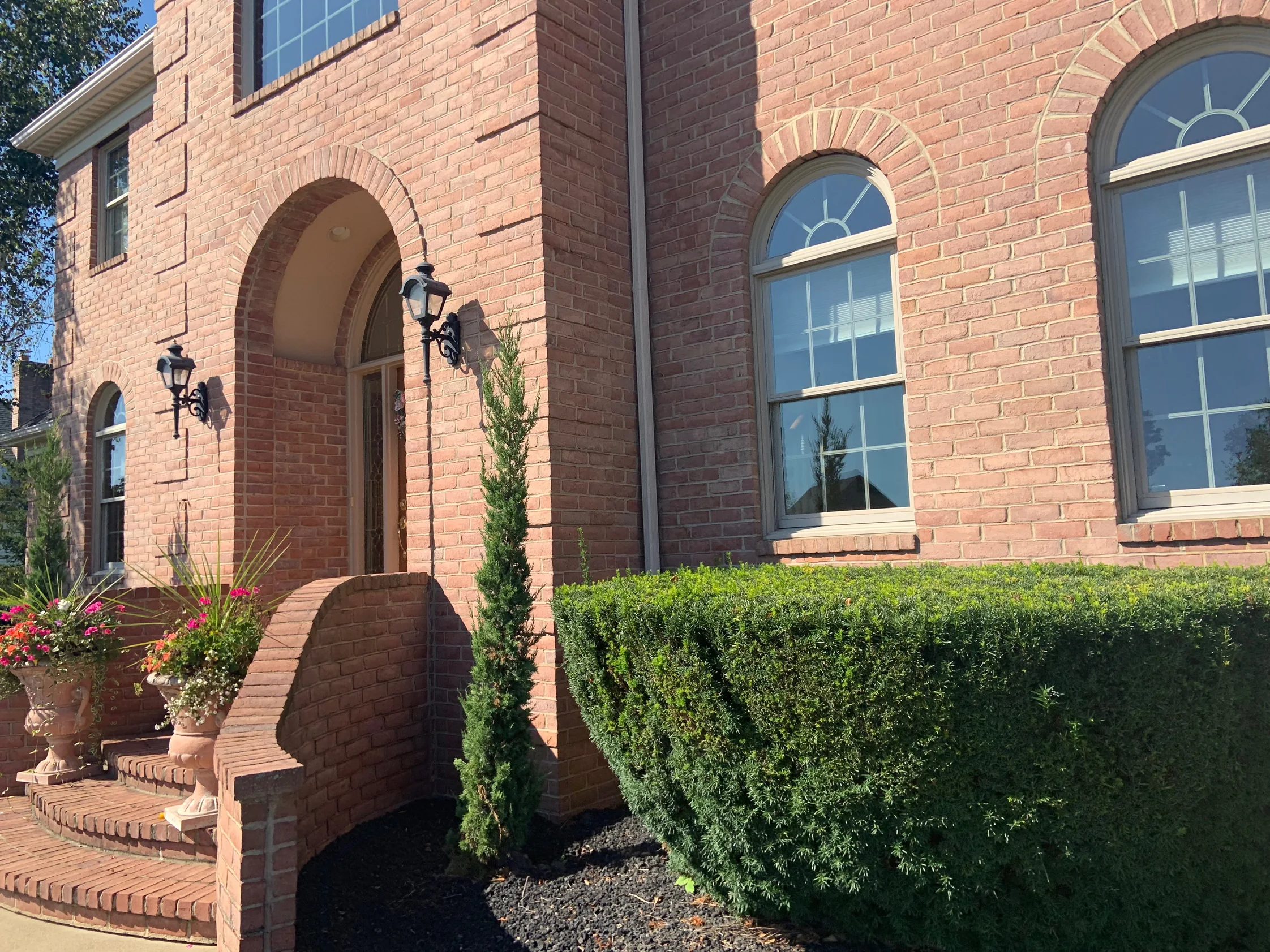 The arched brick entry of the house in 2019, carriage lamps either side of the opening and planted urns on the step, the brick one even warm red range up to the second floor