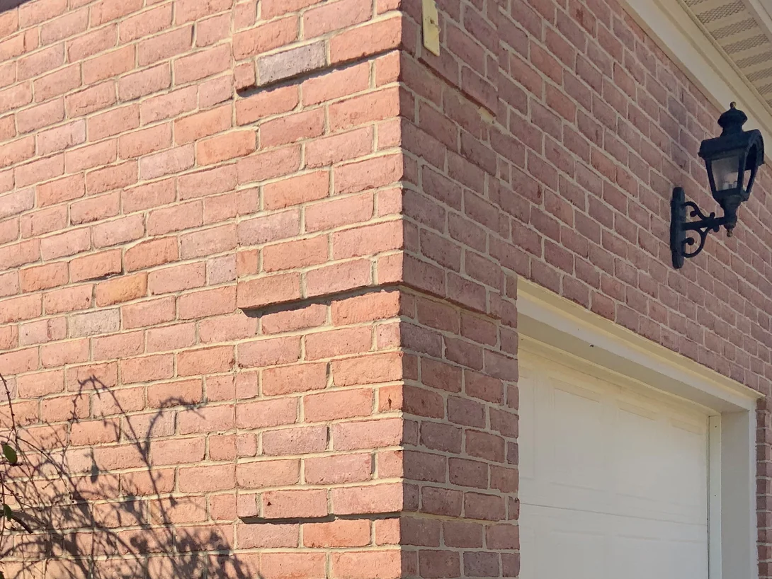 The corner of the garage wing in 2019, carriage lamps above the doors and the brick reading as one even red range across both faces in raking light