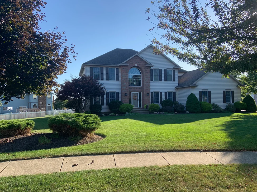 The house seen from the sidewalk in 2019, the brick centre bay reading as one even red, tan and grey blend beside white siding.
