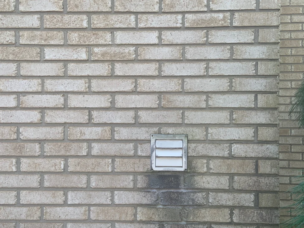 The stained brick at close range in 2019 around a wall vent, the individual units varying slightly in tone within a single blended range