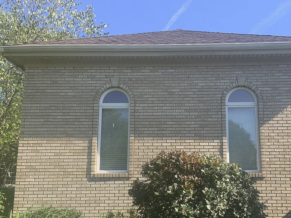 The end wall of the house in 2019, two arched windows under radiating brick arches and the brick around them reading as one even buff and tan blend up to the eaves
