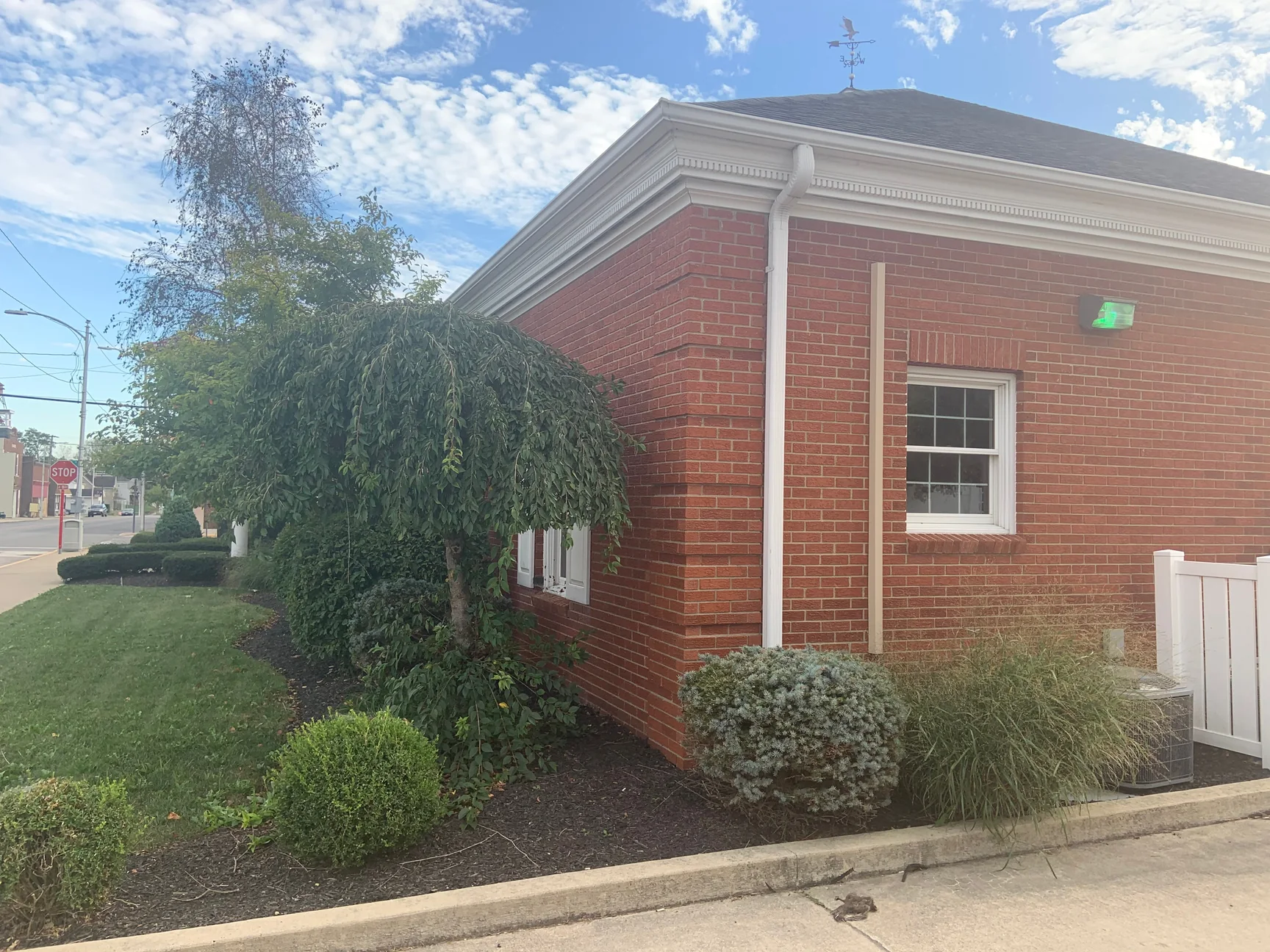 The outside corner of the bank in 2019, red brick running past a quoined corner to a white cornice, with a weeping tree and planted beds along the lawn