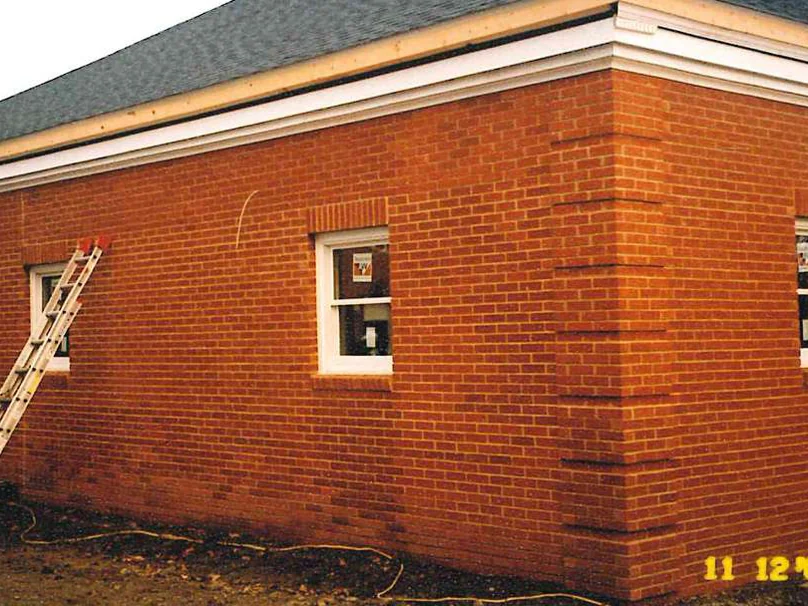 The corner of the bank in 2003 with an extension ladder leaning against the wall beside a window, bare ground along the base and a burned-in camera date in the corner