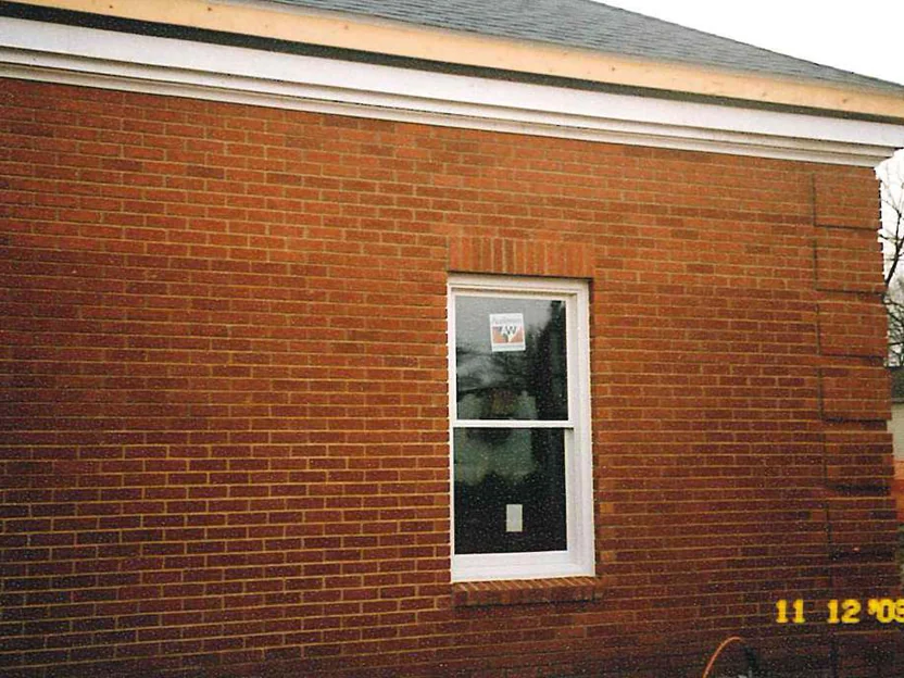 The side wall of the bank in 2003, one white sash window in red brick, with darker runs banding across the courses and a burned-in camera date in the corner