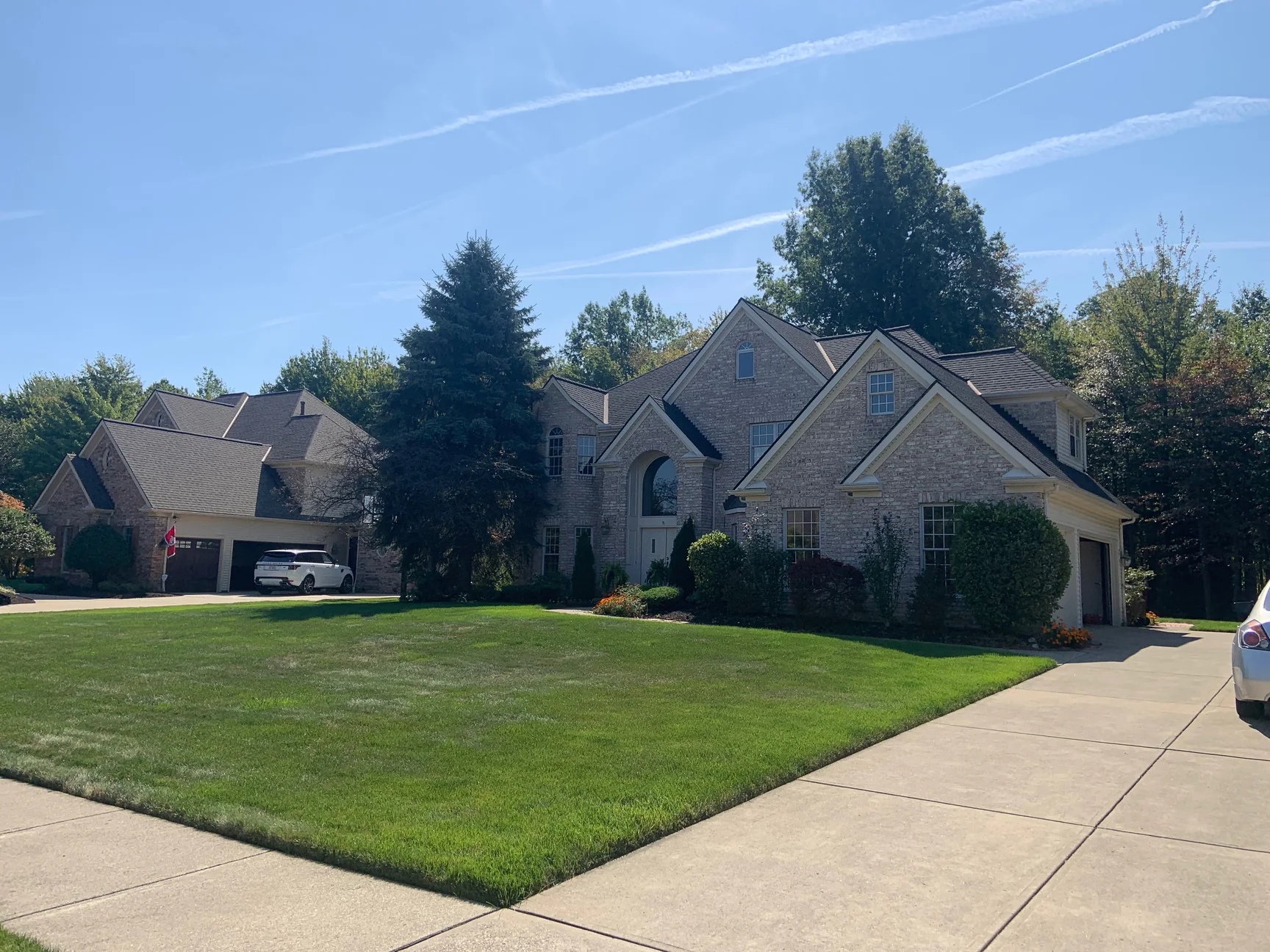 The house seen from the kerb across its front lawn in 2019, the brick reading as one even cream and tan range across the gables and the garage wing