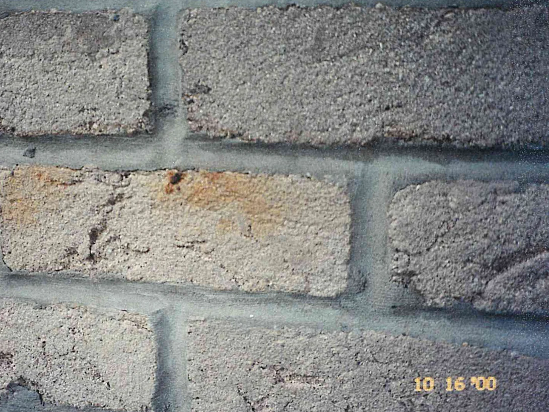 Close view of the brick before the work, most units a dark grey and one pale unit stained orange brown with rust