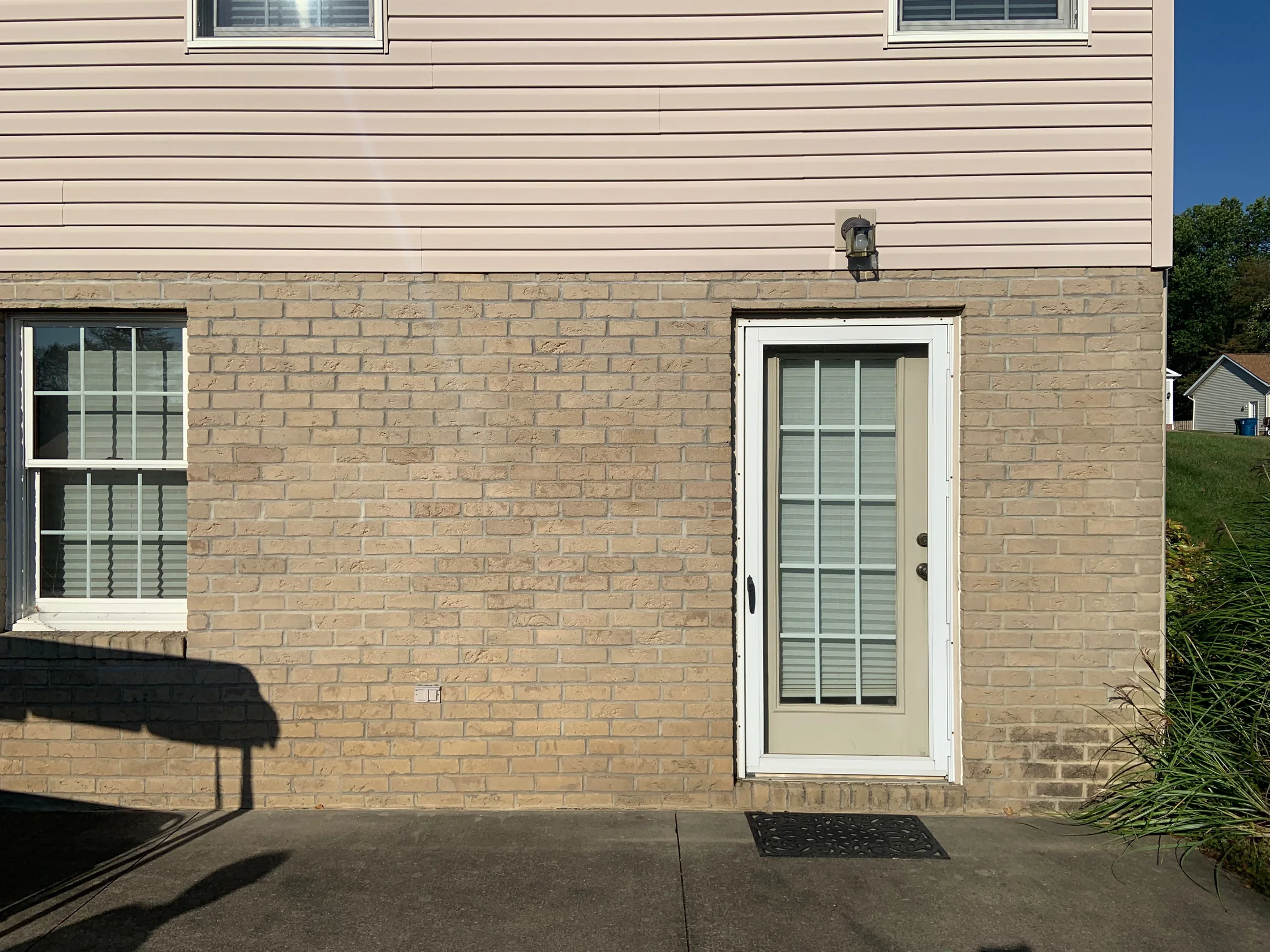 The side door and window of the house in 2019, the buff brick base course running under pale siding as one even range