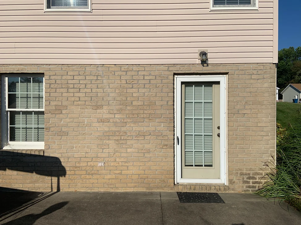 The side door and window of the house in 2019, the buff brick base course running under pale siding as one even range