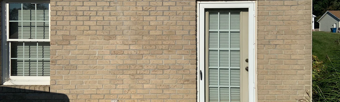 The buff brick base course of an Ohio house in 2019, running past a side door as one even cream and tan range