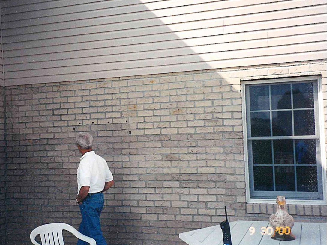 The patio wall part way through the work, a man standing beside a treated stretch of brick that reads lighter than the wall to his left
