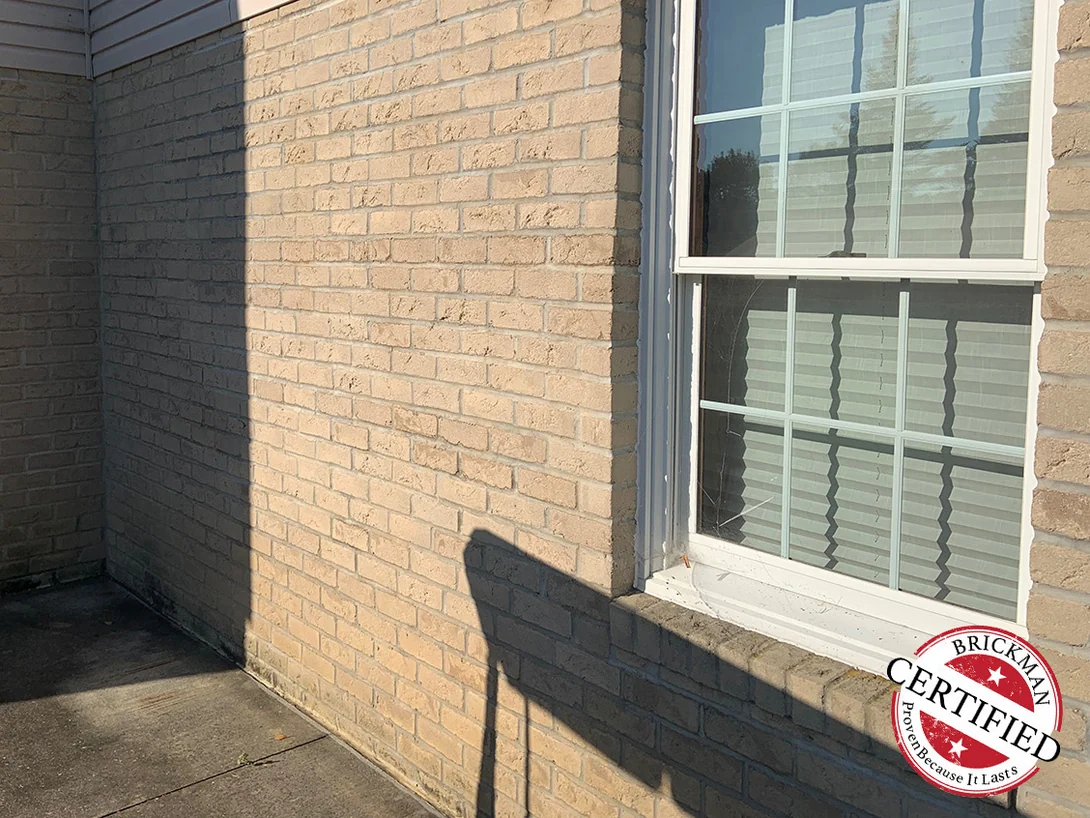 An inside corner of the patio in 2019 beside a window, the brick an even cream and tan range, with the certification stamp at the bottom right