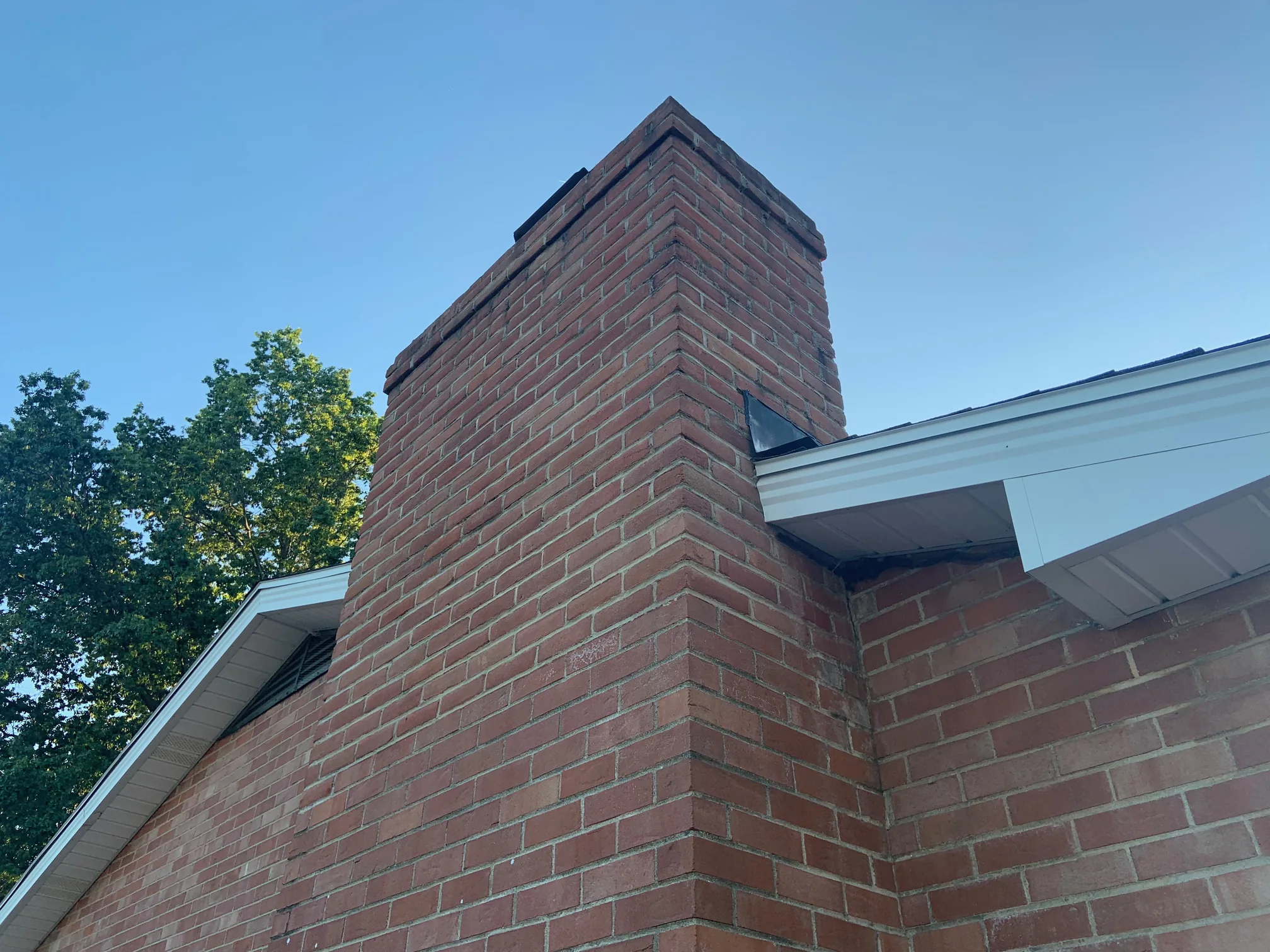 The outside corner of the chimney from below in 2019, the stack and the house wall it stands against carrying the same red and brown brick past the roof edge