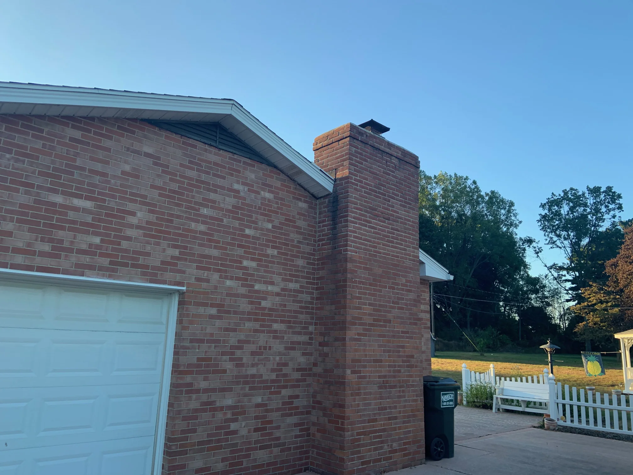The gable end, the garage and the chimney seen from the driveway in 2019, the stack and the wall behind it reading as one red and brown brick range under a white eaves line