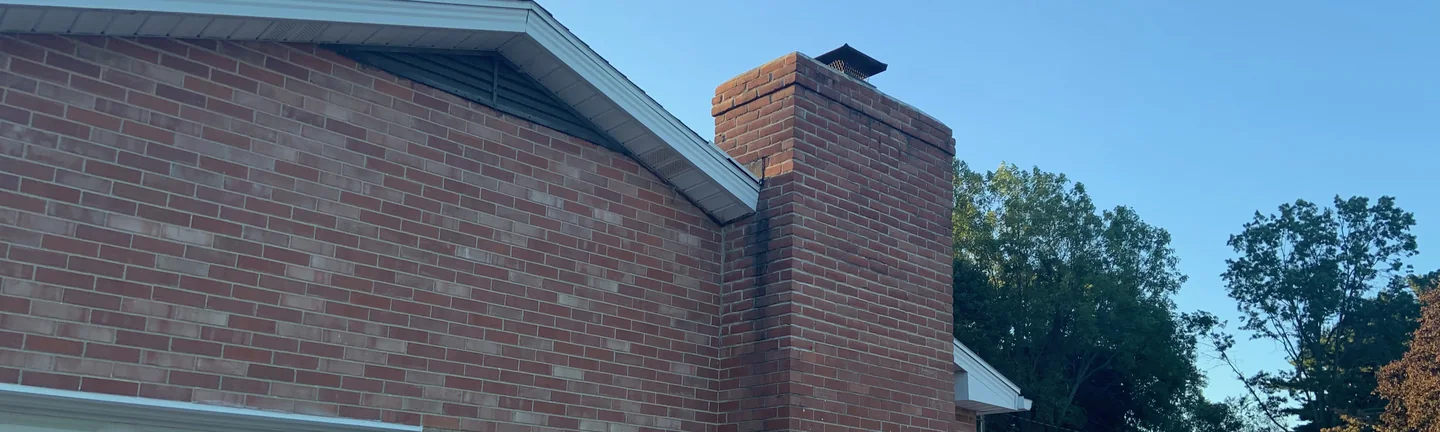 The chimney and the gable end of the house from the driveway in 2019, the stack and the wall reading as one red and brown brick range