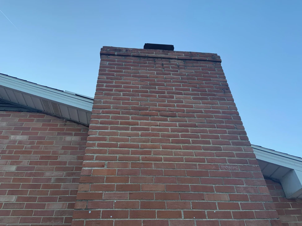 The broad face of the chimney looking up from the ground in 2019, its brick one red and brown range from the shoulder to the corbelled cap and the flue