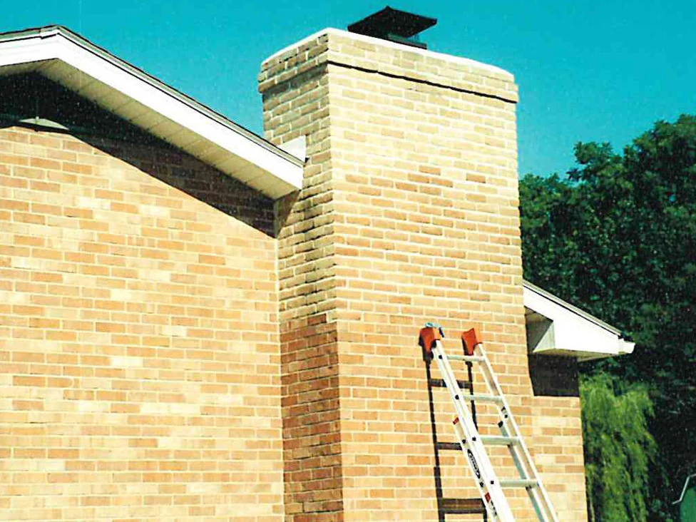 Two extension ladders leaning against the chimney in 2001, the stack now reading in the same tan and orange range as the house wall beside it