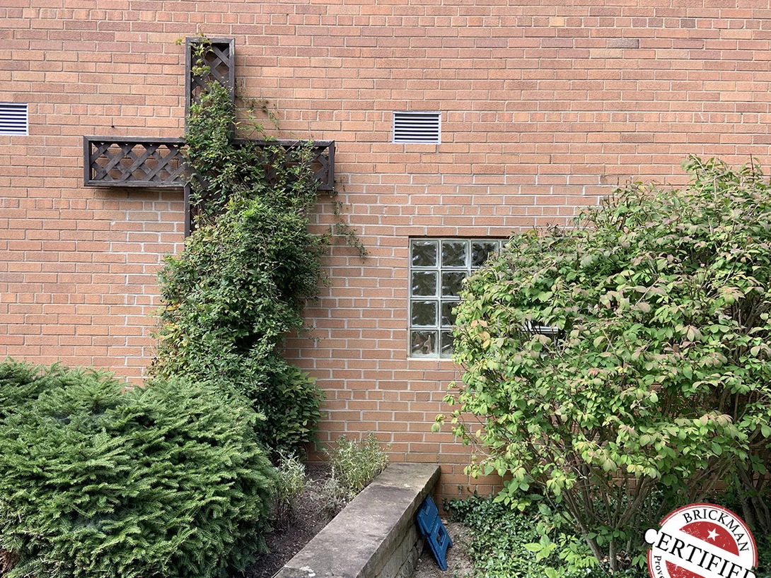A wooden lattice cross fixed to the church's brick wall in 2019, planting grown up around its foot