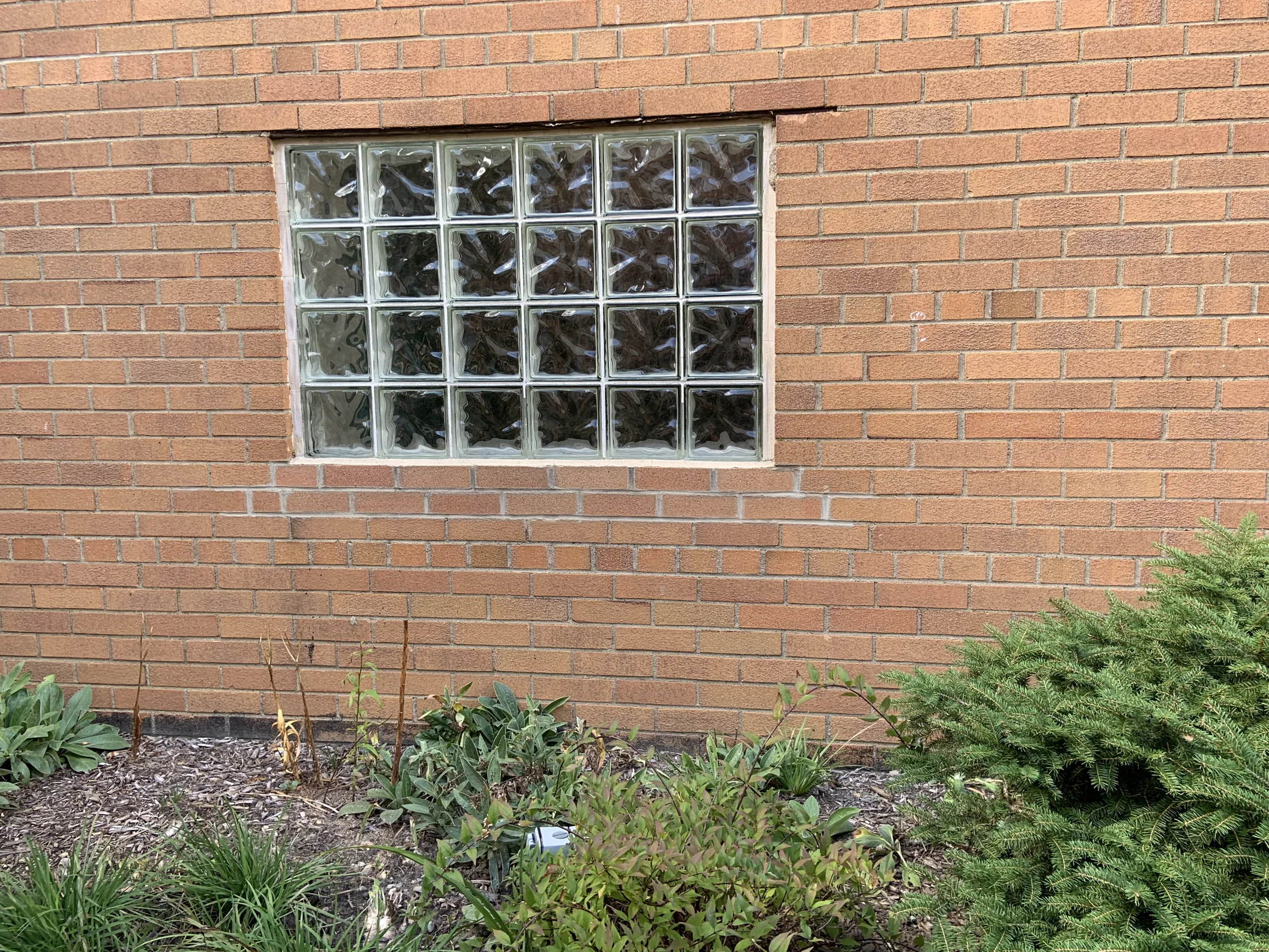 A glass block window set in the church's brick in 2019, the wall around it reading as one even orange range from sill to soldier course