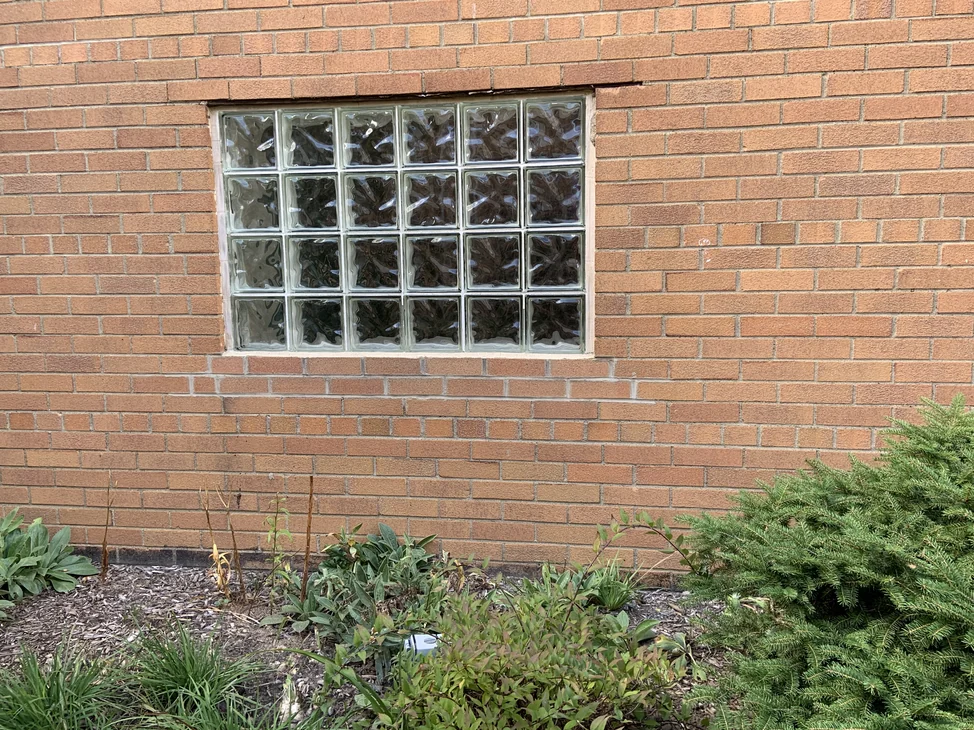 A glass block window set in the church's brick in 2019, the wall around it reading as one even orange range from sill to soldier course.