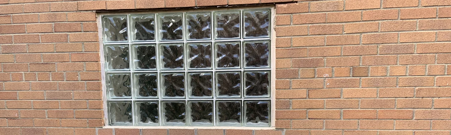 A glass block window set in the church's stained brick in 2019, the units around it reading as one even orange range