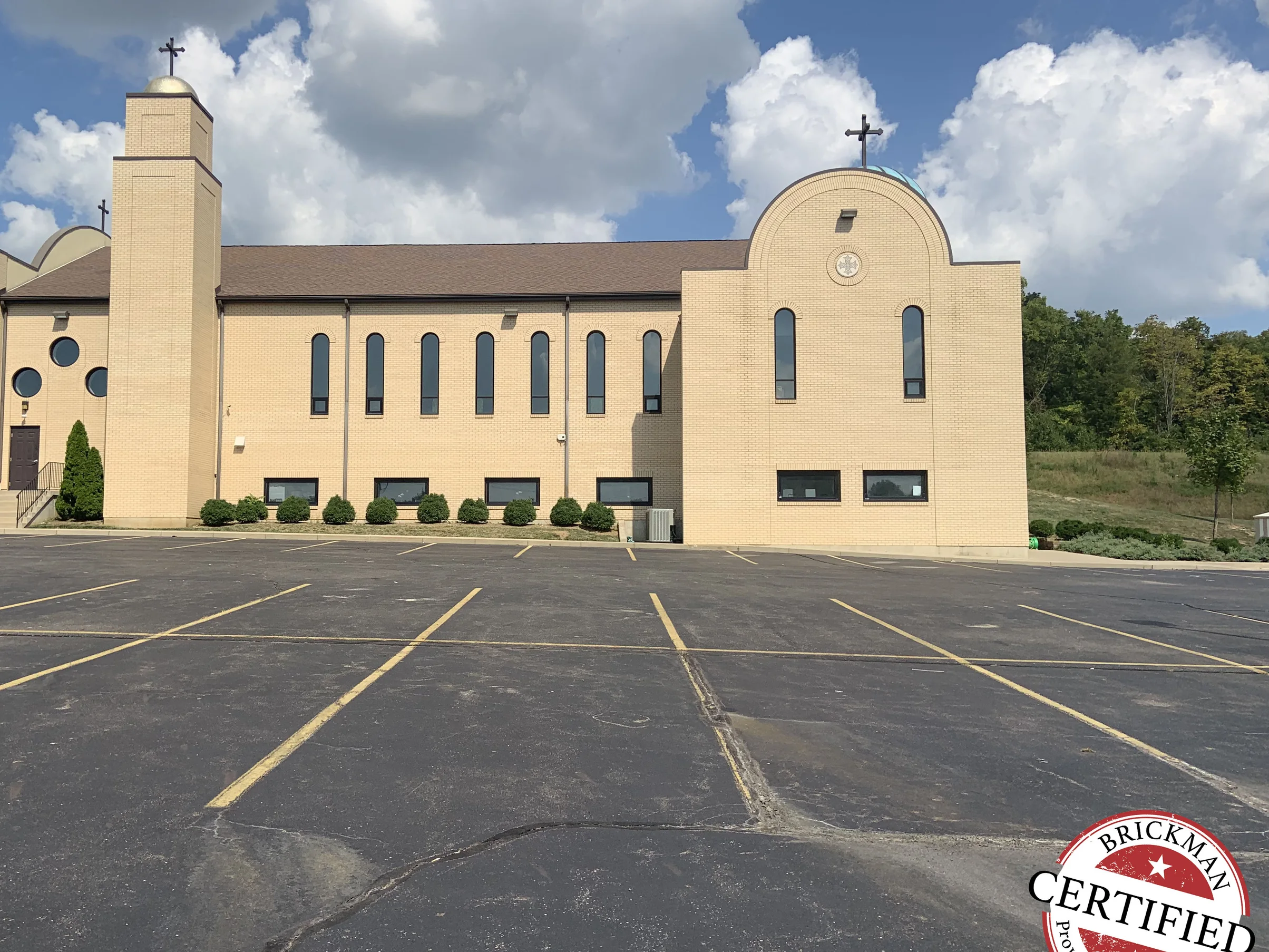 The long side of the church in 2019 seen from across its parking lot, the bell tower, arched gable end and window range all in one even buff brick
