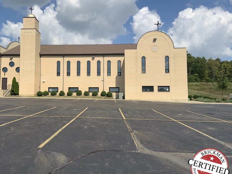 The long side of the church in 2019 seen from across its parking lot, the bell tower, arched gable end and window range all in one even buff brick.