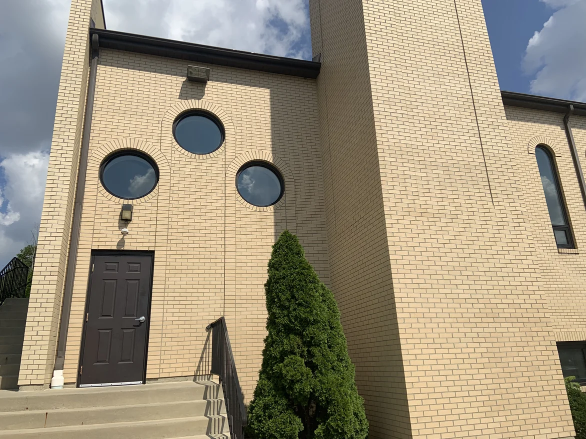 A side entrance below three round windows set in radiating brick arches, the wall carrying on up to the tower beside it