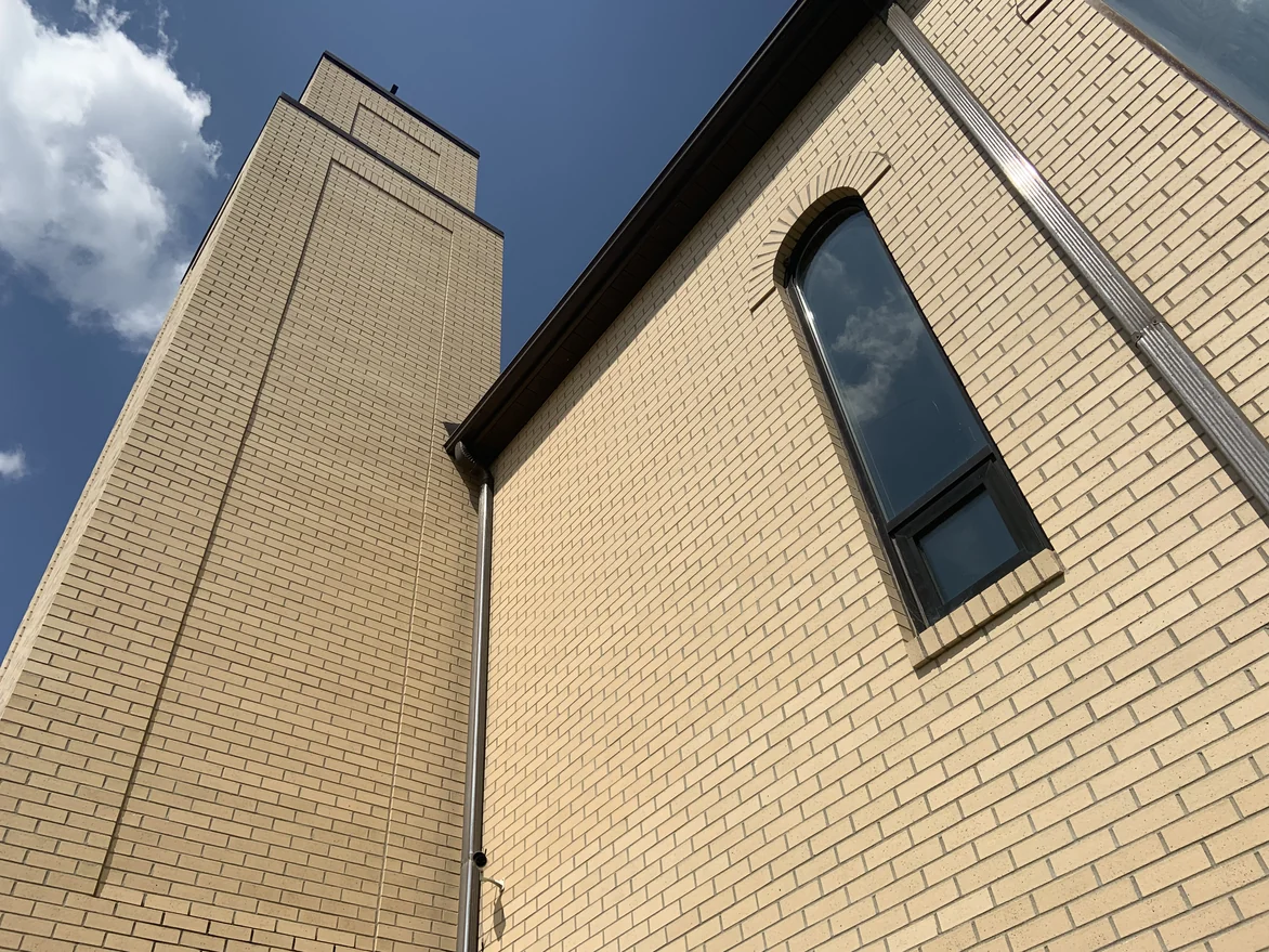 The bell tower seen from its base against a deep blue sky, the brick coursing unbroken to the top beside a tall arched window
