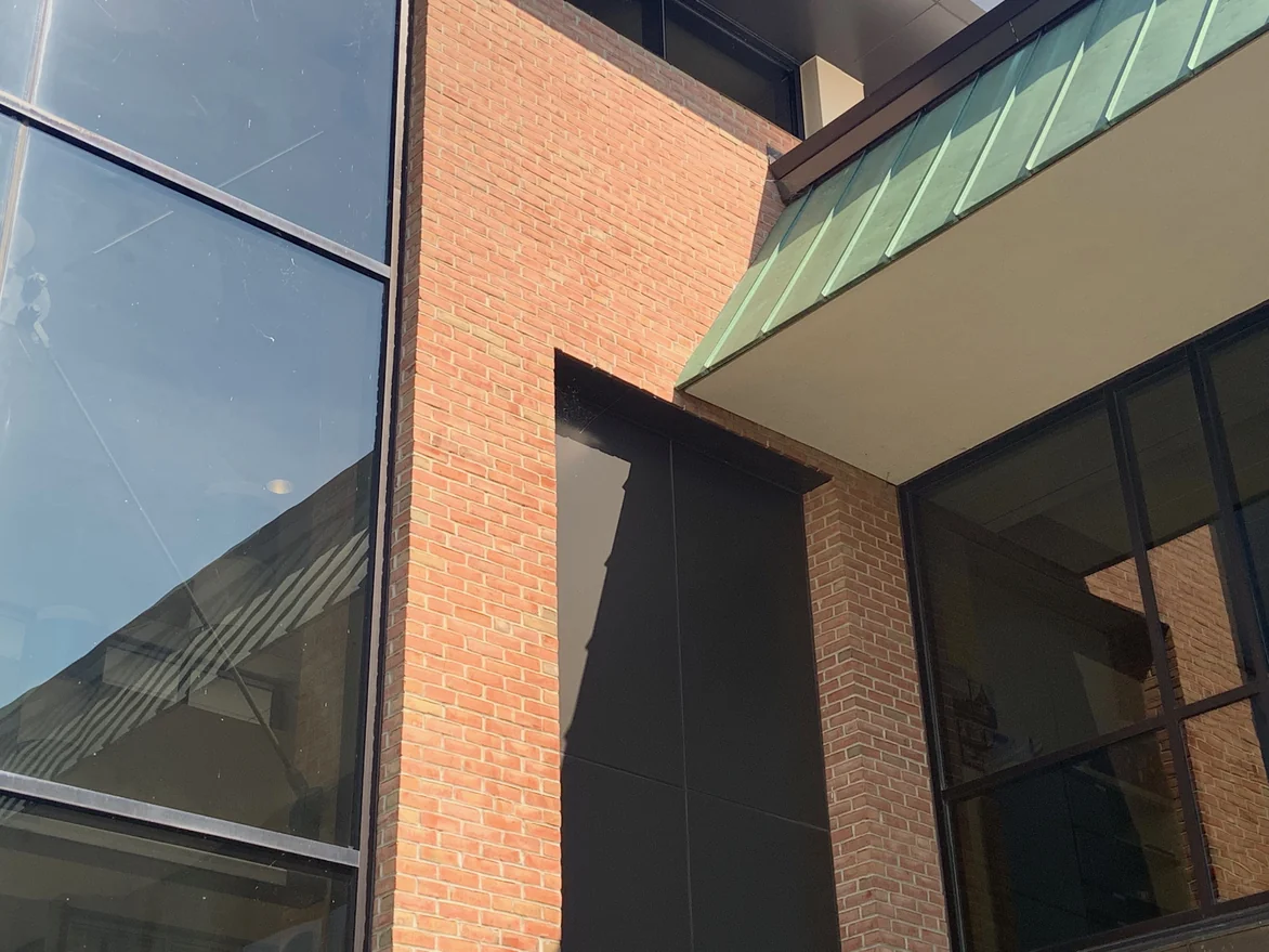 Looking up a brick pier between two glazed bays to a green standing seam fascia over a pale soffit