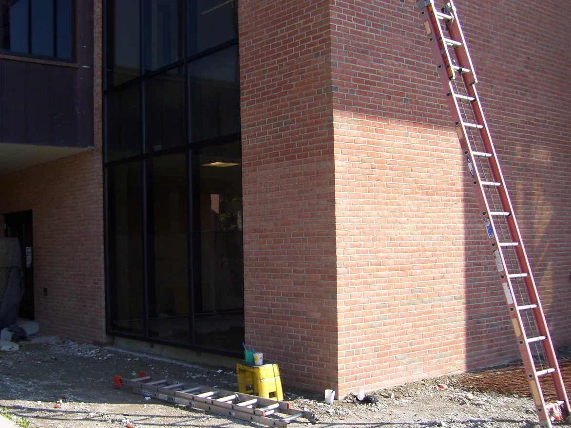 A ladder leaning on the brick corner of the building during the work, a paler washed panel of brick running across the face beside it