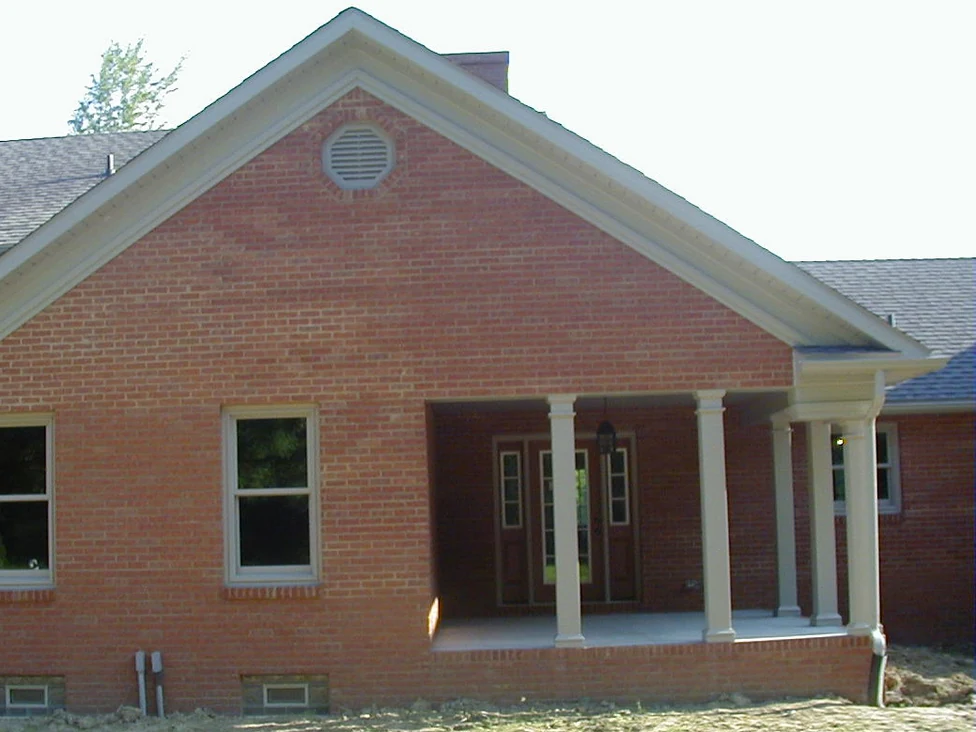The gable end and covered porch of the new house in 2004, the orange red brick broken by pale washed patches and the mortar joints reading as a light grid across it