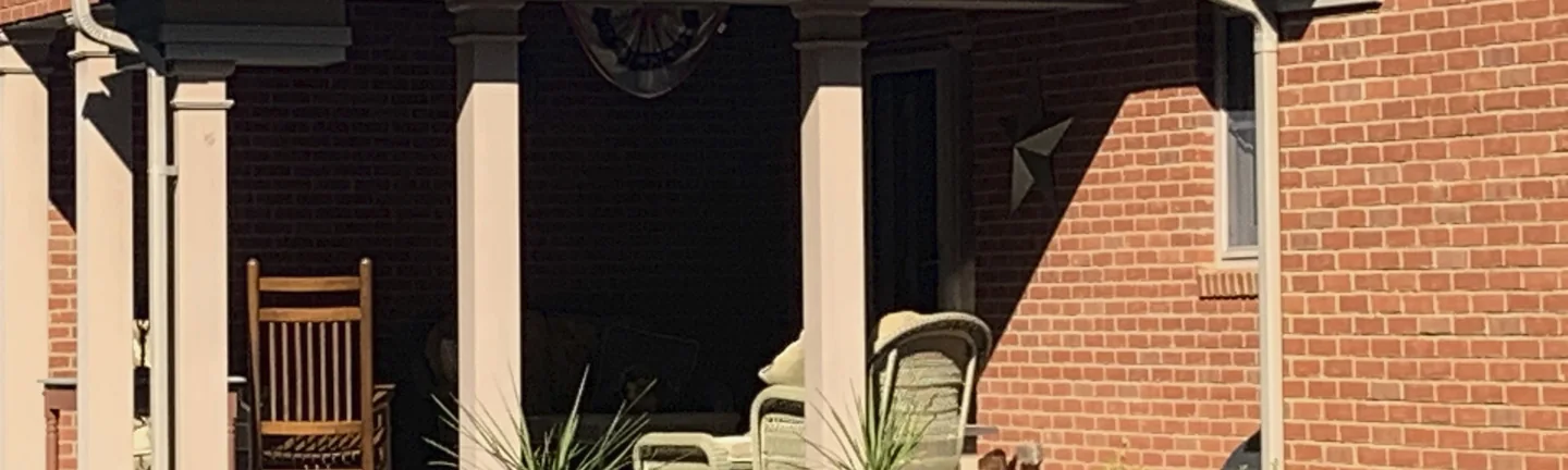 The covered porch of the house in 2019, its columns and the brick wall beside them under a low roof