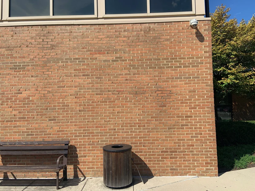 The same wall in 2019 from further back, running from a bench and a timber bin past a dome camera to the window band above