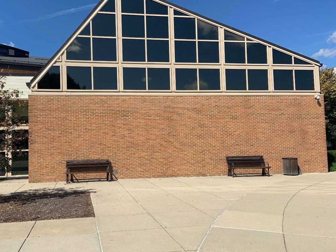 The gable end in 2019, the brick reading as one red brown range from the paving to the glazing, with benches against the wall and mature trees beyond