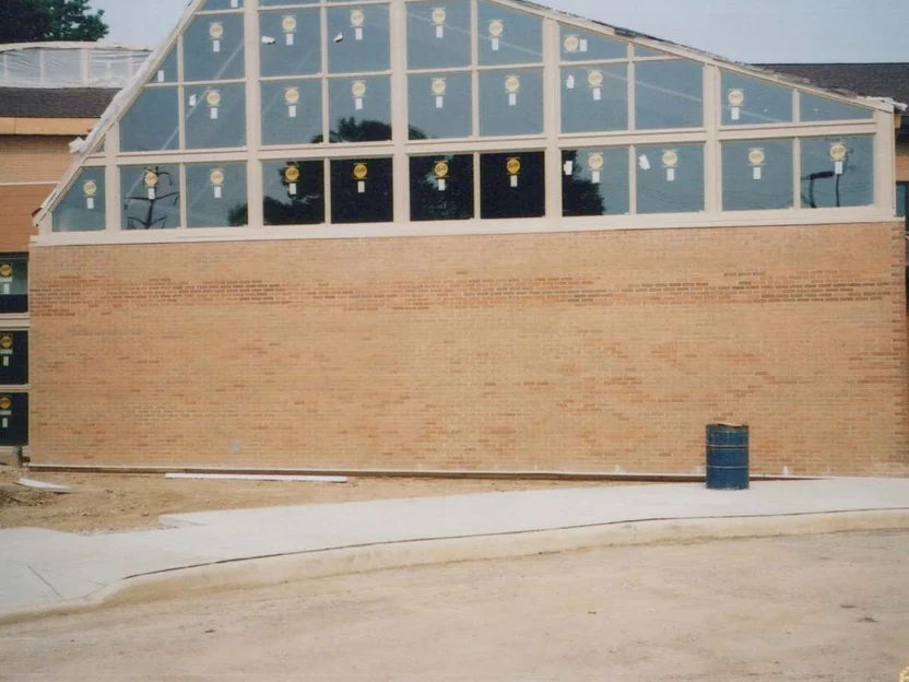 The gable end in 2002, pale buff brick under a sloping wall of dark glazing, with bare graded dirt and a steel drum in front of it