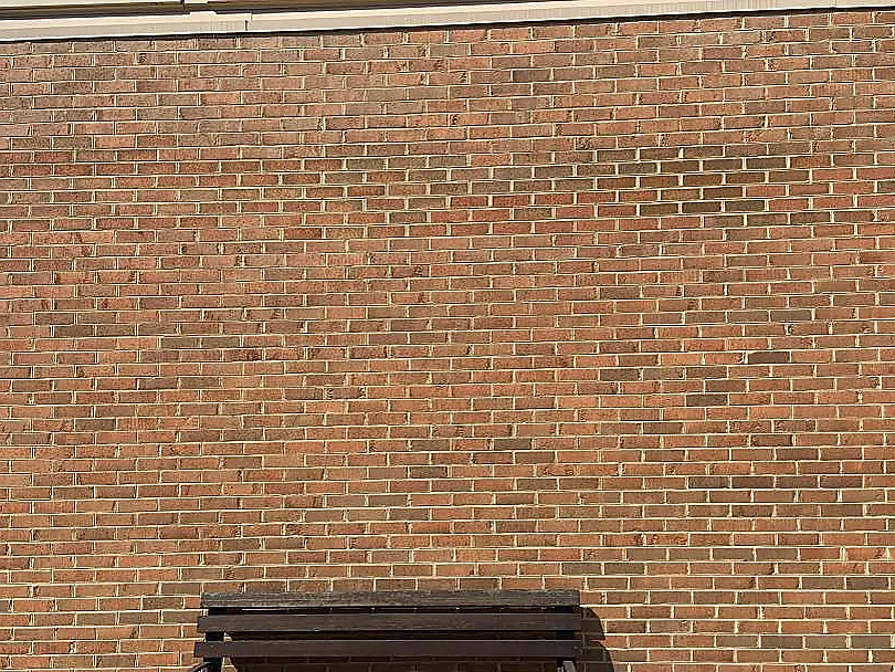 The wall in 2019 square on, every course holding the same red brown range across the full width, a bench standing against the foot of it