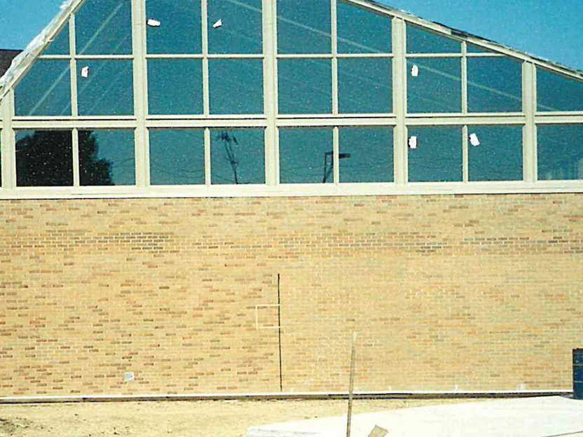 The same wall in 2002 from closer in, the buff brick running the full width below the glazing, a young tree staked in raw ground at the left